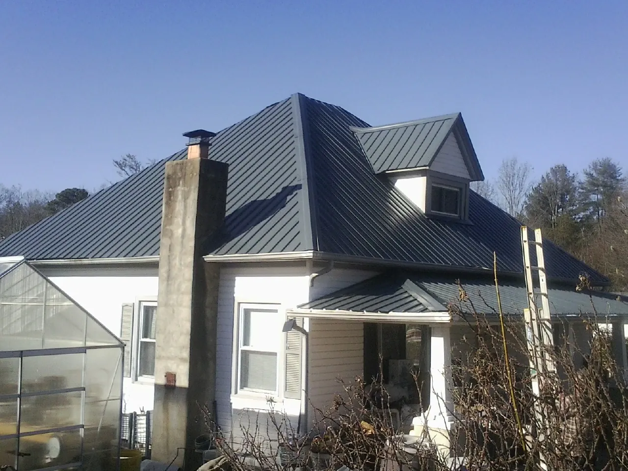 Dark blue standing seam metal roof on a white farmhouse with dormer — Slate & Tile Roof Repair by Roofing Brothers in North Woodstock