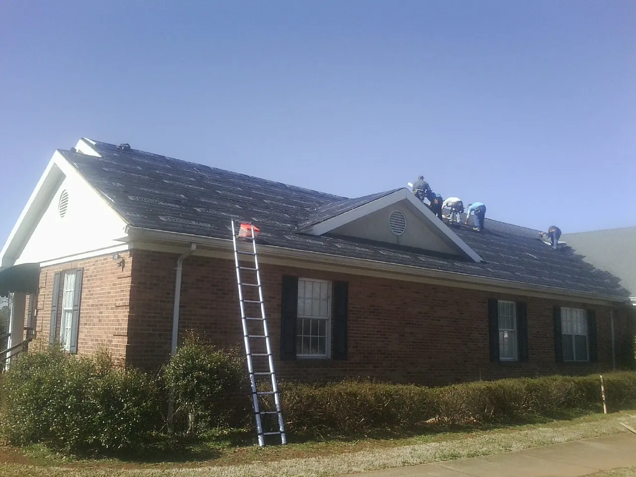 Crew tearing shingles off a brick ranch roof with a ladder set — Metal Roof Repair work by our crew in North Woodstock