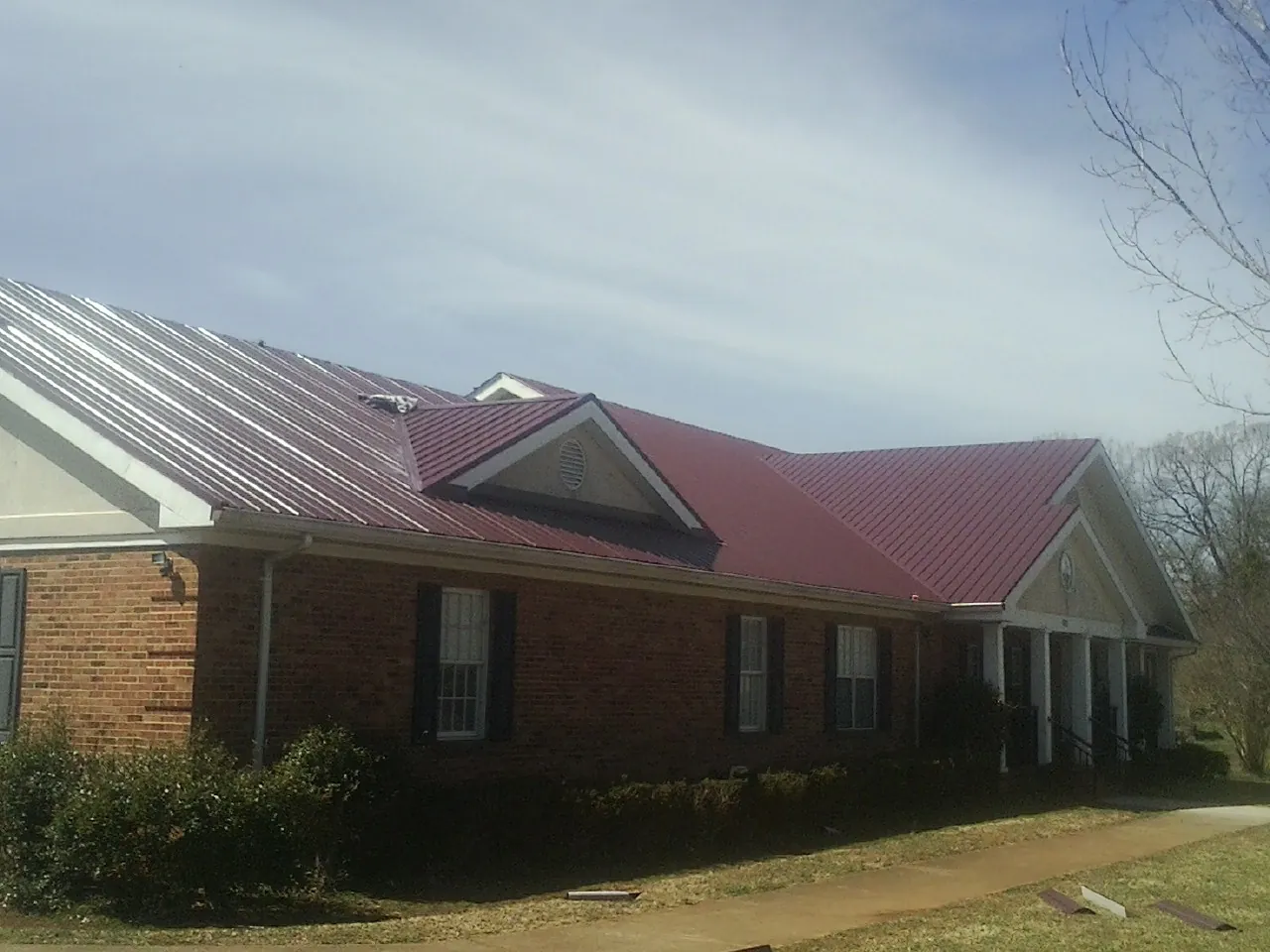 Red metal roof with gabled entries on a long brick building, from a Hail Damage Roof Repair job in North Woodstock