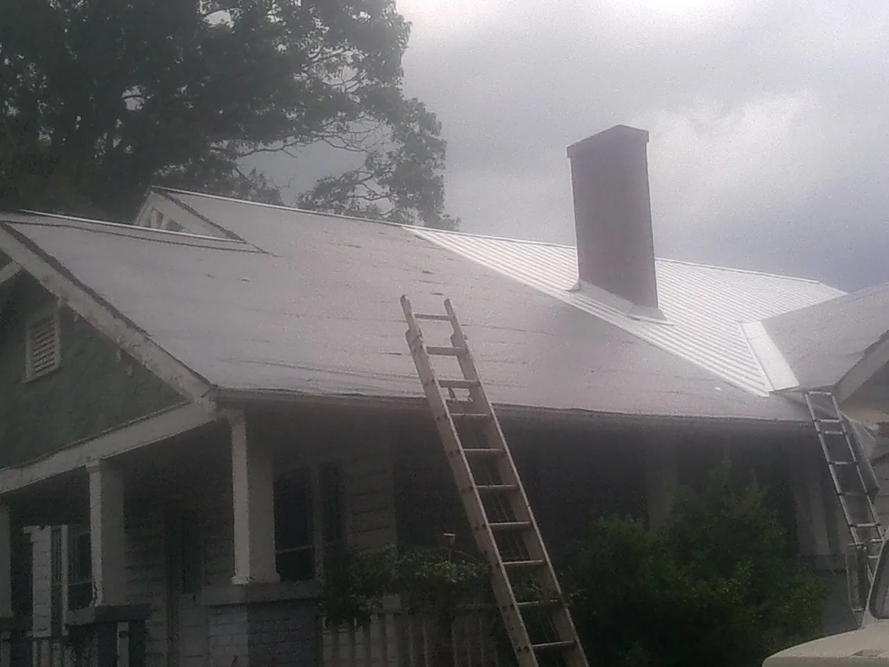 Ladders against a metal roof on an older home with a brick chimney in North Woodstock