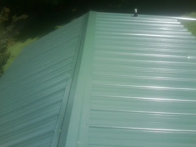 New green metal panels meeting at the ridge of a roof — Flat Roof Repair work by our crew in North Woodstock