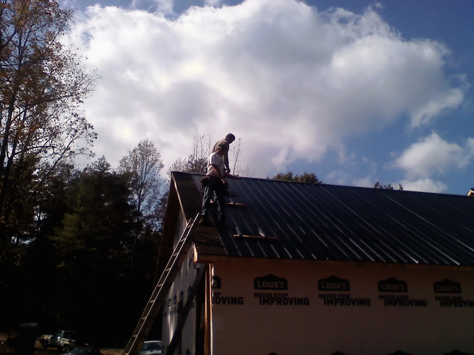 Roofer fastening dark metal panels high against a cloudy sky, from a Roof Inspection job in North Woodstock