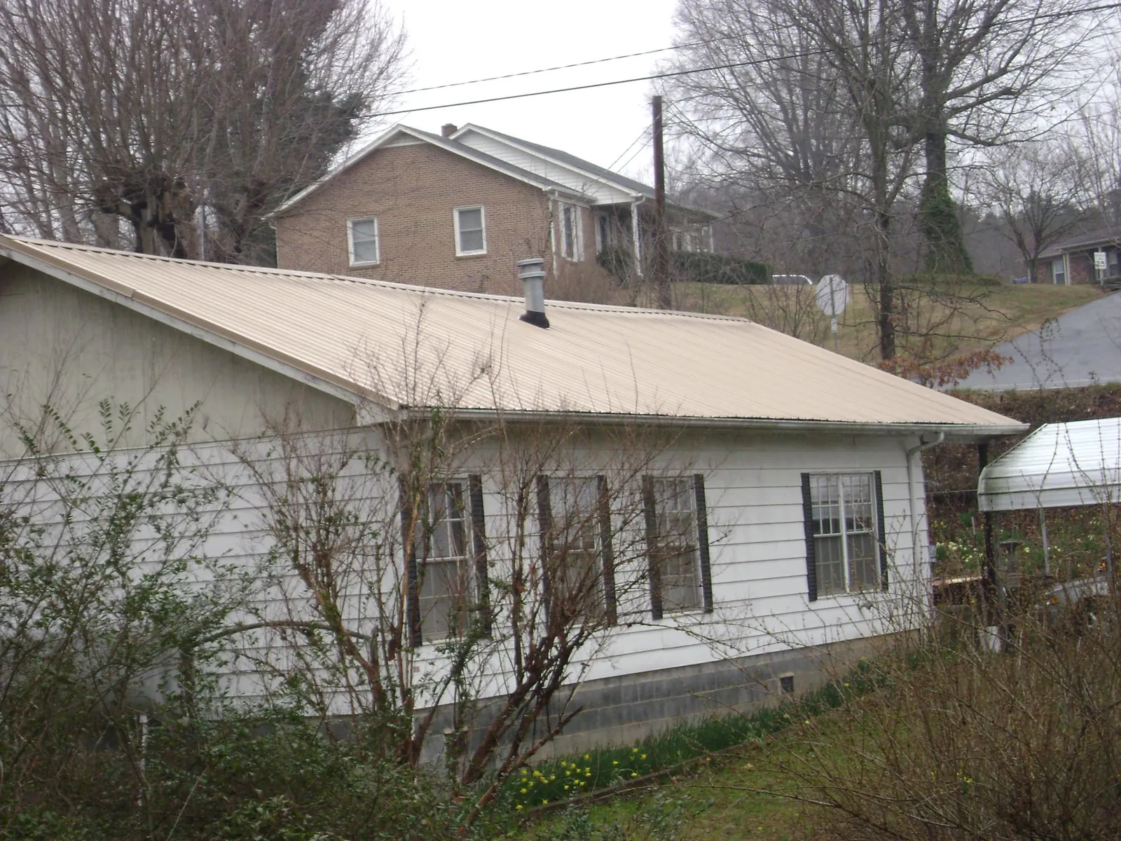Tan metal roof on a white sided house set into a hillside — Commercial Roofing by Roofing Brothers in North Woodstock