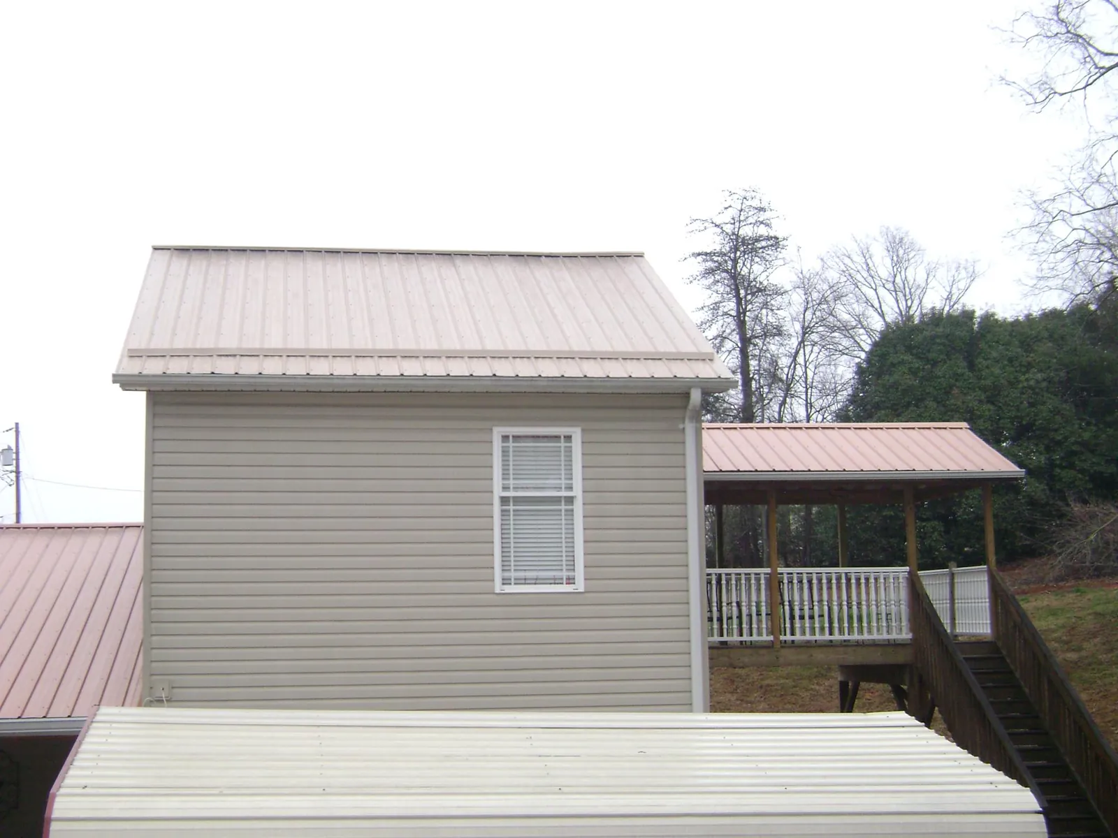 Tan metal roofs on a two story addition and attached porch, from a Roof Replacement job in North Woodstock
